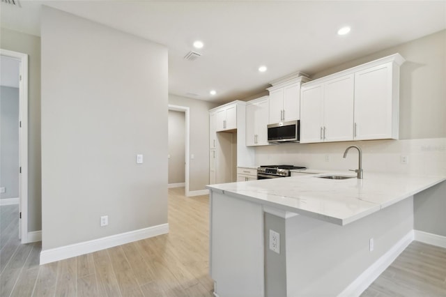 kitchen with kitchen peninsula, stainless steel appliances, sink, light wood-type flooring, and white cabinetry