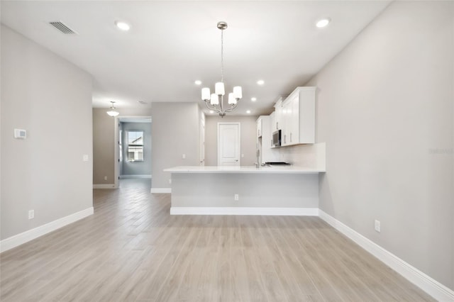 kitchen featuring kitchen peninsula, light hardwood / wood-style floors, pendant lighting, white cabinets, and an inviting chandelier