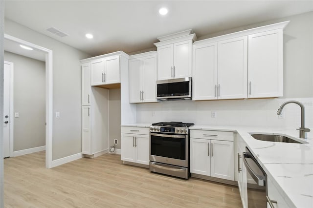 kitchen with appliances with stainless steel finishes, white cabinets, sink, and light wood-type flooring