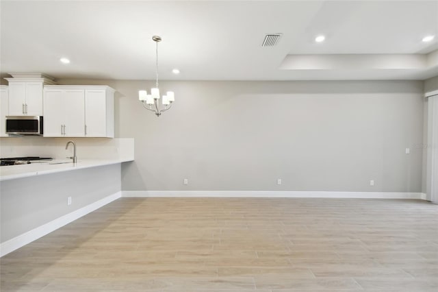 kitchen with white cabinets, a chandelier, sink, light hardwood / wood-style floors, and decorative light fixtures