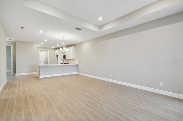 unfurnished living room featuring a notable chandelier and light hardwood / wood-style floors