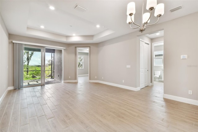 empty room featuring a chandelier, light hardwood / wood-style flooring, and a raised ceiling