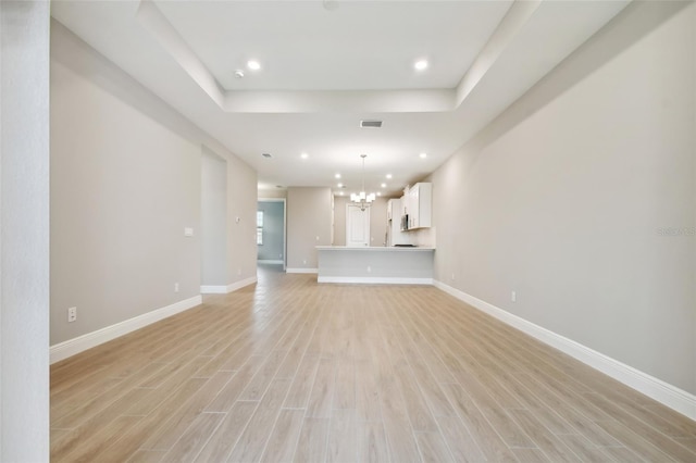 unfurnished living room featuring light hardwood / wood-style floors, a tray ceiling, and an inviting chandelier