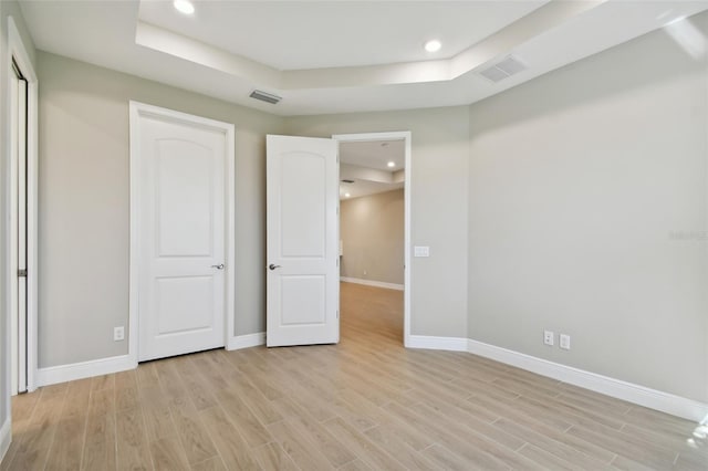 unfurnished bedroom with a tray ceiling and light hardwood / wood-style floors