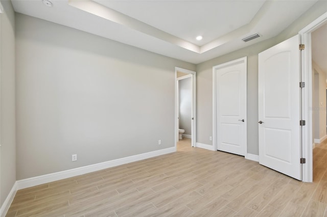 unfurnished bedroom with light hardwood / wood-style flooring, ensuite bathroom, and a raised ceiling