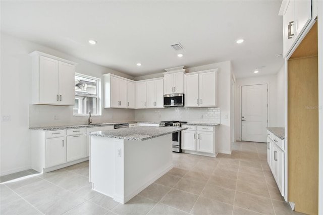 kitchen featuring stainless steel appliances, white cabinetry, light stone countertops, light tile patterned floors, and a center island