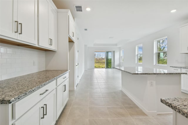 kitchen with white cabinets, light tile patterned flooring, light stone counters, and a center island