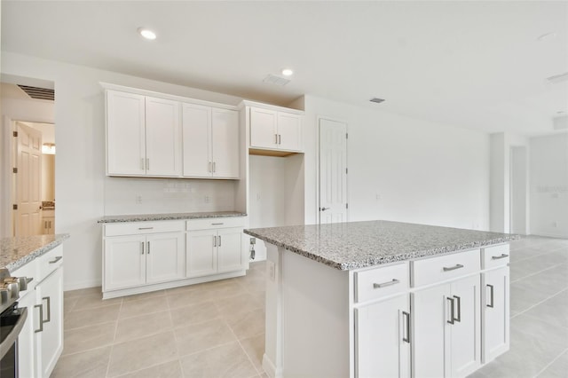 kitchen featuring light tile patterned flooring, white cabinetry, light stone countertops, backsplash, and a kitchen island