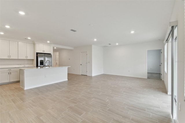 kitchen with sink, white cabinets, stainless steel fridge, a kitchen island with sink, and light hardwood / wood-style floors