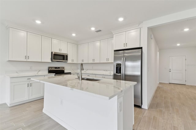 kitchen featuring appliances with stainless steel finishes, white cabinetry, sink, a kitchen island with sink, and light stone counters