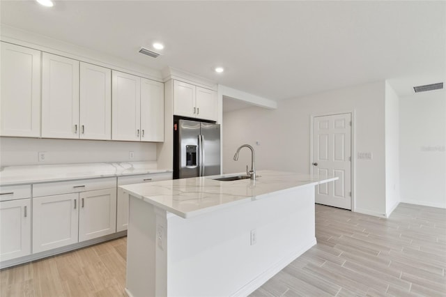 kitchen featuring sink, stainless steel fridge, white cabinetry, light hardwood / wood-style floors, and a center island with sink