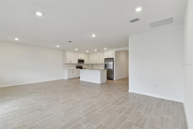 interior space with sink, appliances with stainless steel finishes, white cabinetry, an island with sink, and light wood-type flooring