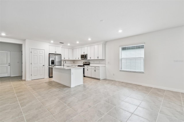 kitchen with sink, light tile patterned floors, stainless steel appliances, an island with sink, and white cabinets