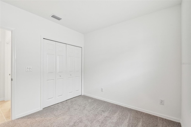 unfurnished bedroom with light colored carpet and a closet