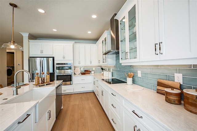 kitchen with hanging light fixtures, white cabinetry, stainless steel appliances, and wall chimney exhaust hood