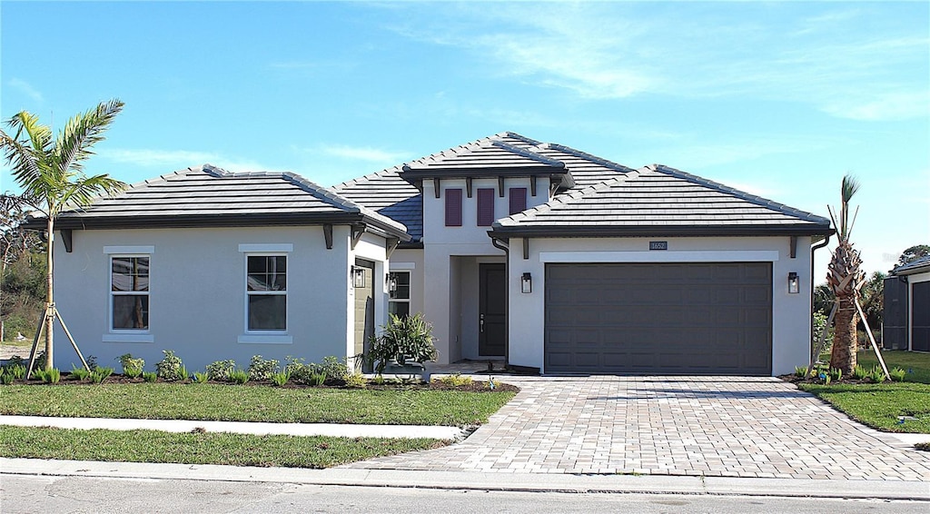 view of front of property with a garage, a tile roof, decorative driveway, a front lawn, and stucco siding