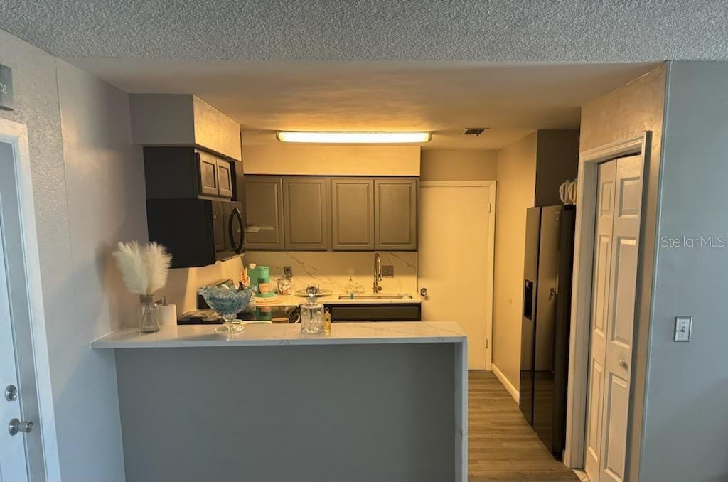 kitchen with kitchen peninsula, hardwood / wood-style floors, sink, gray cabinetry, and stainless steel appliances