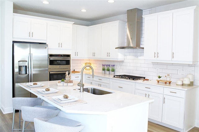 kitchen featuring sink, white cabinets, stainless steel appliances, a center island with sink, and wall chimney exhaust hood