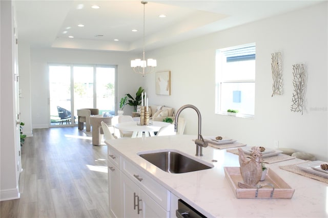 kitchen with sink, white cabinetry, hanging light fixtures, a raised ceiling, and light stone countertops