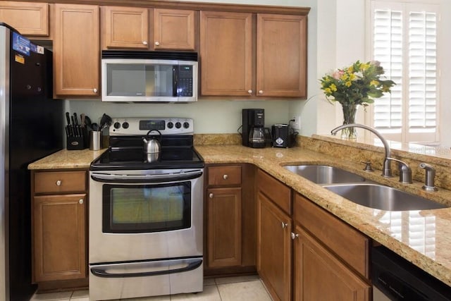 kitchen featuring appliances with stainless steel finishes, a sink, brown cabinets, light tile patterned floors, and light stone counters
