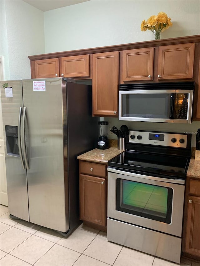 kitchen featuring appliances with stainless steel finishes, light tile patterned floors, and brown cabinets