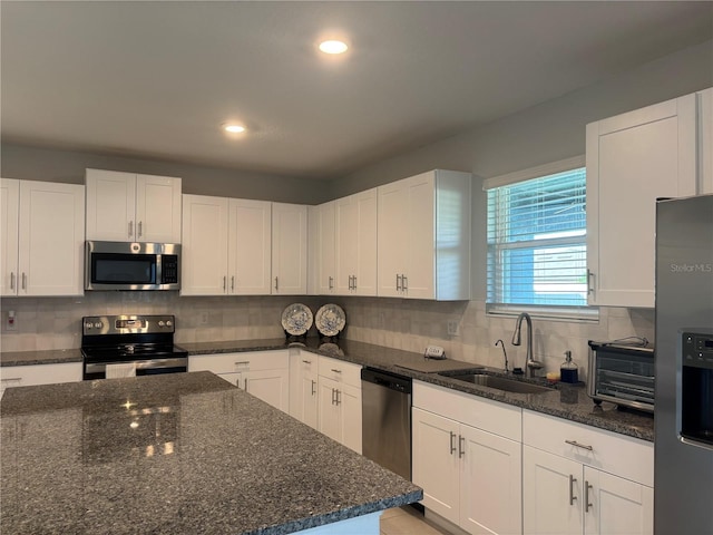 kitchen with dark stone counters, white cabinets, appliances with stainless steel finishes, and a sink