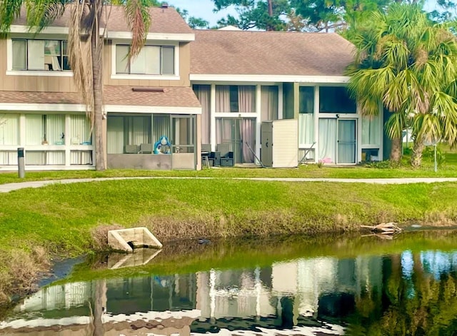 rear view of property featuring a yard, a shingled roof, and a water view