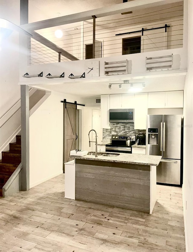 kitchen featuring a barn door, tasteful backsplash, appliances with stainless steel finishes, light stone counters, and light wood-style floors