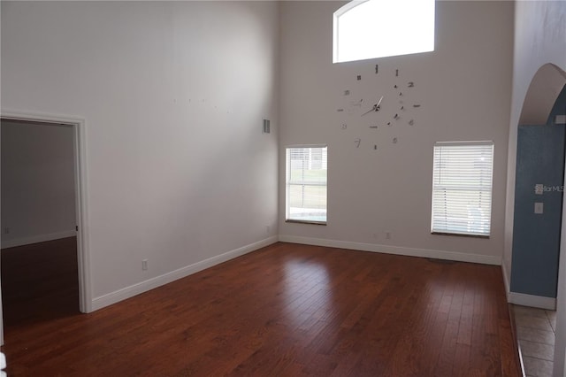 unfurnished living room featuring a towering ceiling, a wealth of natural light, and dark wood-type flooring