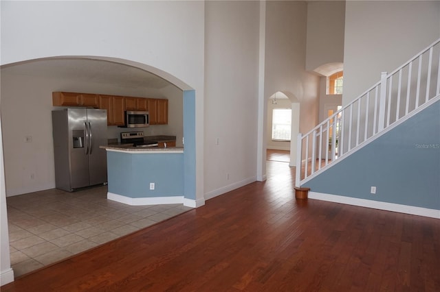 kitchen featuring light wood-type flooring, a towering ceiling, and appliances with stainless steel finishes