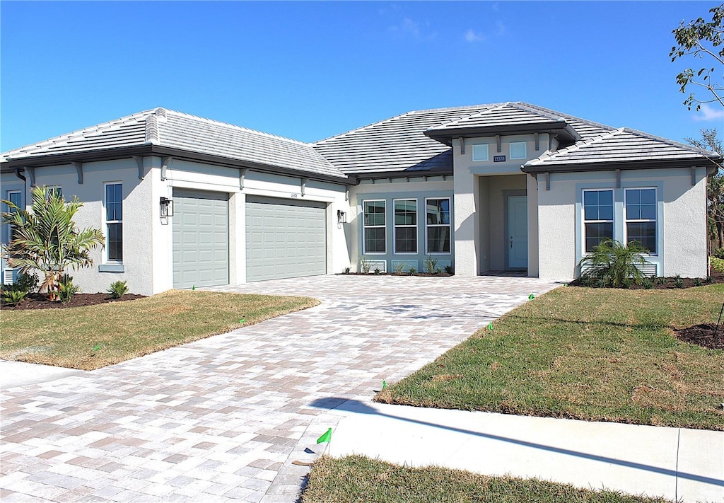 prairie-style home featuring decorative driveway, a tile roof, stucco siding, a front yard, and a garage