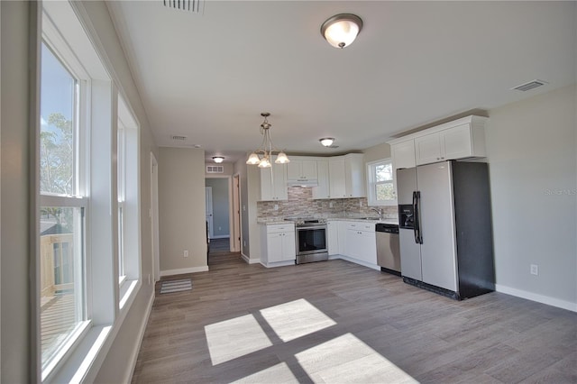 kitchen with white cabinetry, stainless steel appliances, light hardwood / wood-style floors, and decorative light fixtures