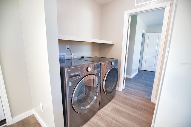 laundry room with washing machine and clothes dryer and light hardwood / wood-style floors