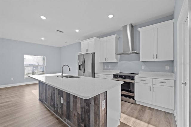 kitchen with wall chimney exhaust hood, light wood-type flooring, an island with sink, and appliances with stainless steel finishes