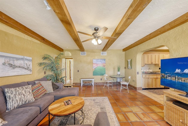 living room featuring beam ceiling, ceiling fan, and a textured ceiling