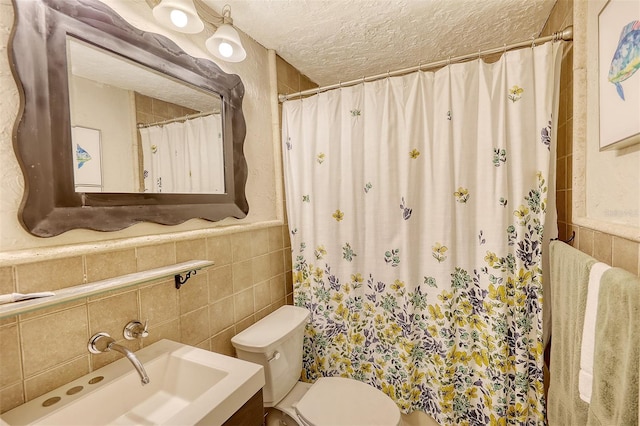 bathroom with a textured ceiling, vanity, tile walls, and toilet