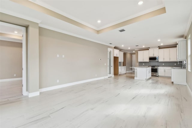 kitchen with appliances with stainless steel finishes, tasteful backsplash, a tray ceiling, a center island, and white cabinetry