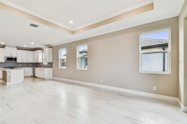 kitchen featuring a raised ceiling, white cabinets, backsplash, a kitchen island, and appliances with stainless steel finishes