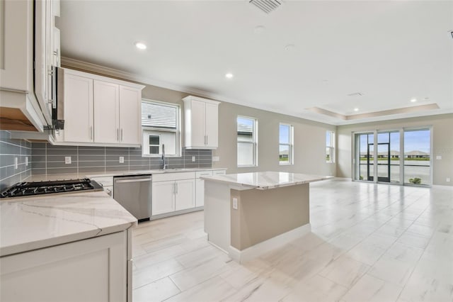 kitchen featuring light stone countertops, stainless steel dishwasher, a tray ceiling, a kitchen island, and white cabinetry