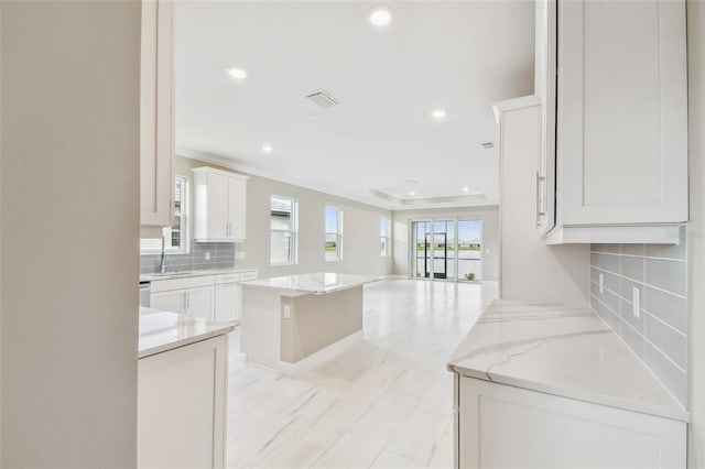 kitchen featuring white cabinets, a kitchen island, light stone counters, and tasteful backsplash