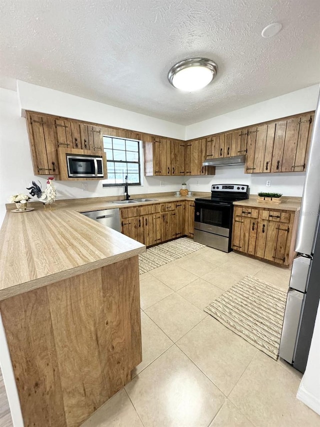 kitchen featuring sink, a textured ceiling, appliances with stainless steel finishes, light tile patterned flooring, and kitchen peninsula