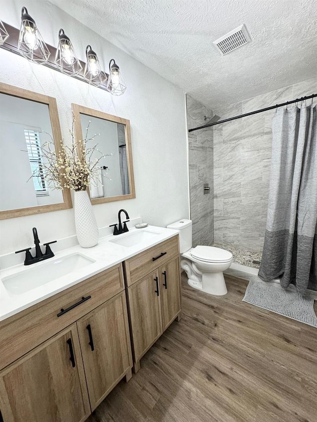 bathroom featuring vanity, hardwood / wood-style flooring, a shower with shower curtain, toilet, and a textured ceiling