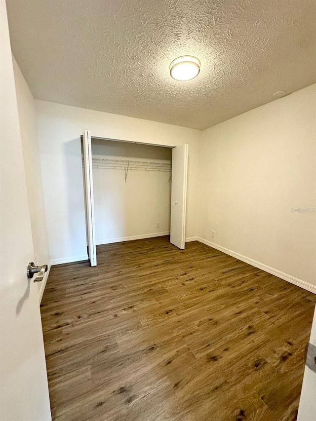 unfurnished bedroom featuring a textured ceiling, a closet, and dark wood-type flooring