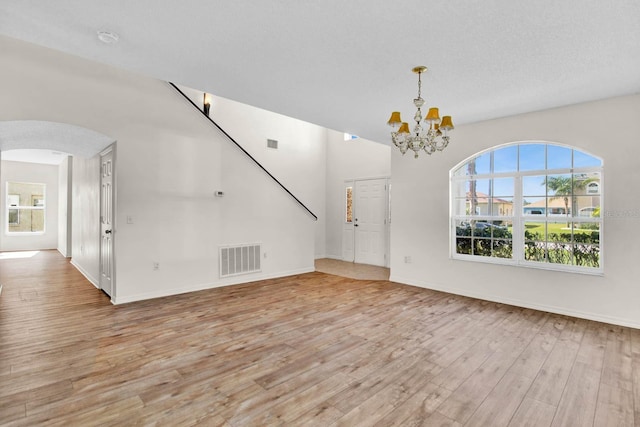 unfurnished living room featuring a textured ceiling, light hardwood / wood-style floors, and a notable chandelier