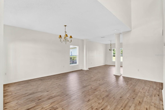 empty room featuring hardwood / wood-style flooring, plenty of natural light, ornate columns, and an inviting chandelier