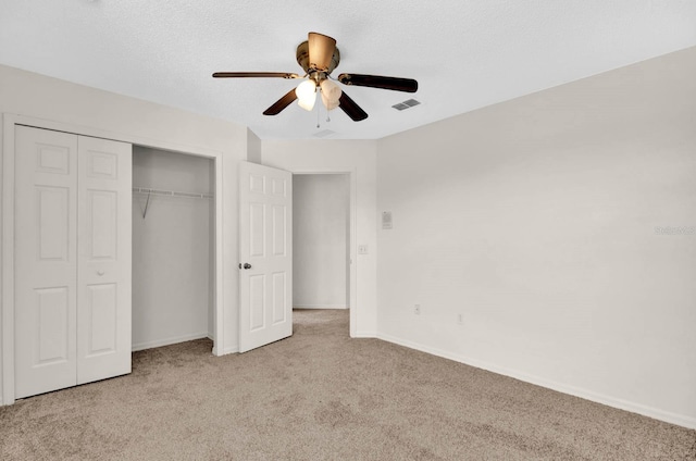 unfurnished bedroom featuring a textured ceiling, a closet, light colored carpet, and ceiling fan