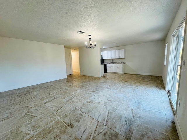 unfurnished living room with a notable chandelier, sink, and a textured ceiling