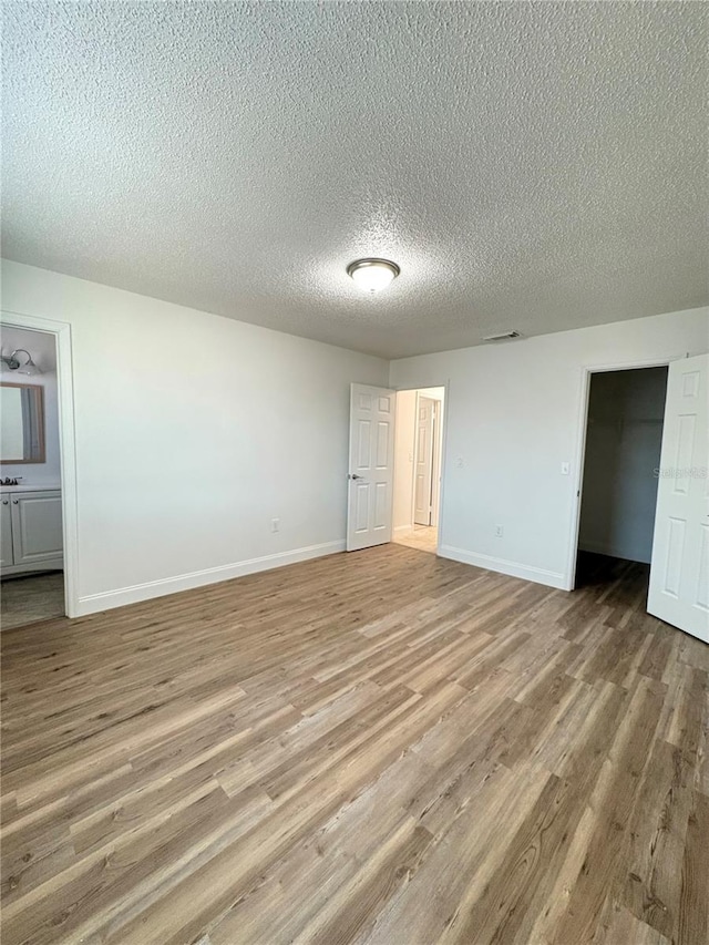 unfurnished bedroom with a textured ceiling, light wood-type flooring, a closet, and connected bathroom