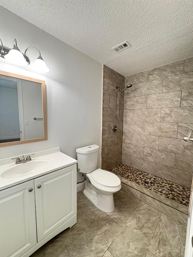 bathroom featuring a tile shower, vanity, a textured ceiling, and toilet