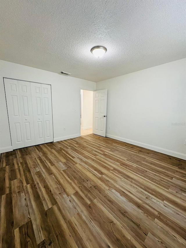 unfurnished bedroom with wood-type flooring, a textured ceiling, and a closet